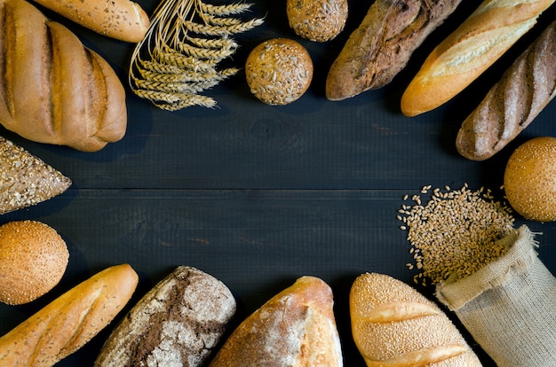 Auswahl an Brot mit Weizenkörnern auf dunklem Hintergrund mit Kopienraum für Ihren Text. Ansicht von oben.