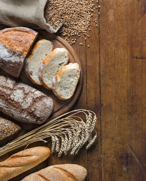 Auswahl an Brotprodukten, Ährchen und Weizenkörnern auf Holztisch mit Kopienraum für Ihren Text. Rustikaler Stil, Ansicht von oben.