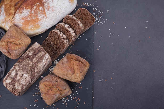 Auswahl an gebackenem Brot auf dunklem Hintergrund. Bäckerei- und Lebensmittelgeschäft-Konzept. Draufsicht mit Platz für Text