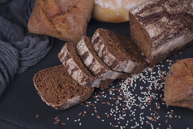 Auswahl an gebackenem Brot auf dunklem Hintergrund. Geschnittenes Roggenbrot. Bäckerei- und Lebensmittelgeschäft-Konzept. Ansicht von oben