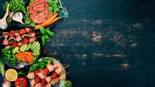 Auswahl an gebackenem Grillfleisch Würstchenspieße frisches Gemüse Tomaten Zwiebeln Knoblauch Auf einem hölzernen Hintergrund Kopieren Sie Platz