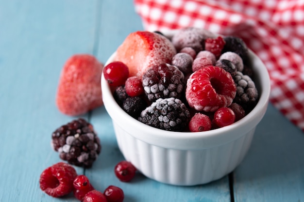 Auswahl an gefrorenen Beeren in einer Schüssel auf blauem Holztisch