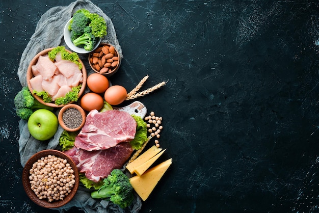 Auswahl an gesunden Proteinquellen und Bodybuilding-Lebensmitteln. Fleisch, Hähnchenfilet, Brokkoli, Bohnen, Käse, Eier, Weizen. Auf einem Steinhintergrund.