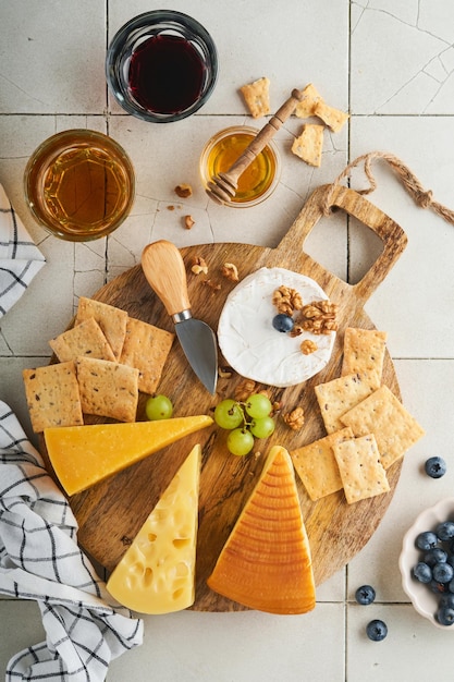 Auswahl an Käse-Honig-Cracker-Heidelbeeren-Trauben mit Rot- und Weißwein in Gläsern Antipasti-Server auf weißem Marmorbrett auf grauem Hintergrund Käseplatte Flacher Kopienraum