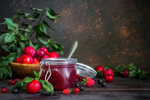 Auswahl an Marmeladen in Gläsern, saisonalen frischen Beeren und Obstpflaumen