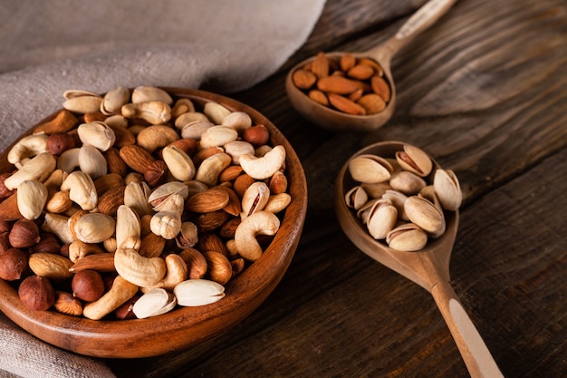 Auswahl an Nüssen in Holzschale auf dunklem Holztisch. Cashew, Haselnüsse, Mandeln und Pistazien.