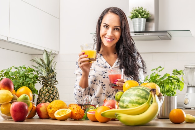 Auswahl an Obst und ein Mädchen, das zwei Tassen roten und gelben Saft hält.