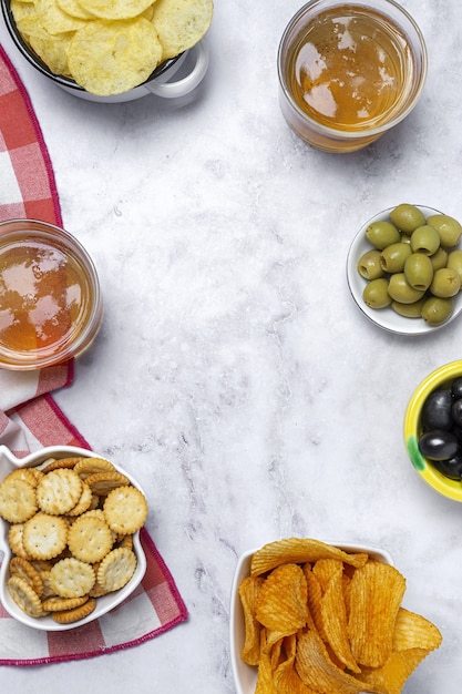 Auswahl an Snacks zu Hause mit Kartoffelchips, Bier, Crackern, grünen und schwarzen Oliven auf Marmortisch