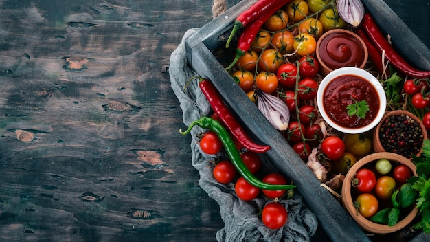 Auswahl an Tomatensaucen in einer Holzkiste Ketchup Kirschtomaten Gewürze Chilischoten Olivenöl Petersilie Ansicht von oben