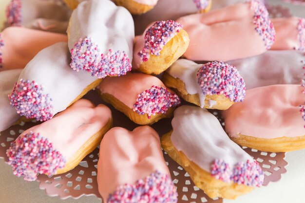 Auswahl an traditionellen französischen Eclairs. Platte mit Profitroles mit rosa Zuckerguss für Party-Dessert-Stand. Candy Bar und Catering-Konzept für Geburtstag, Hochzeit und andere Feiertagsfeiern, Nahaufnahme