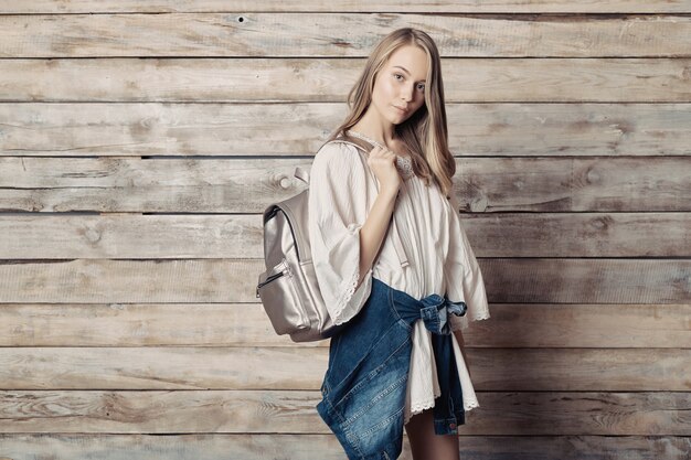 Auténtica joven rubia con mochila plateada sobre pared de madera