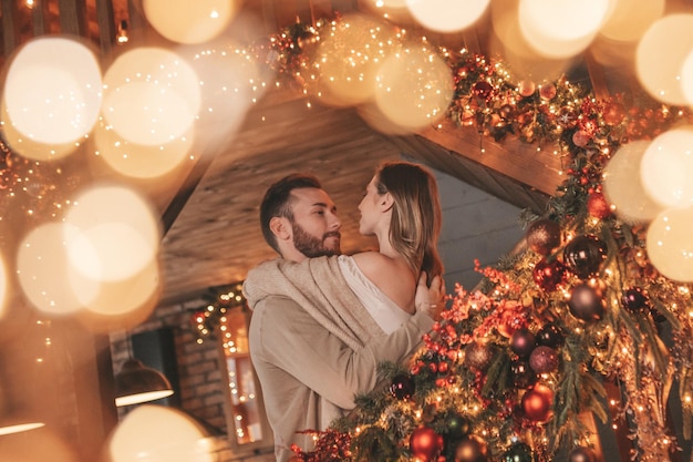 Auténtica y sincera pareja casada feliz pasando tiempo juntos en un albergue de madera decorado con Navidad