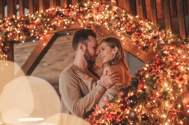 Auténtica y sincera pareja casada feliz pasando tiempo juntos en un albergue de madera decorado con Navidad