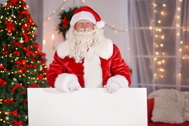 Auténtico Papá Noel con cartel en habitación decorada para Navidad