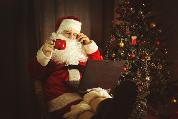 Auténtico Papá Noel está trabajando en una computadora portátil Interior de la casa