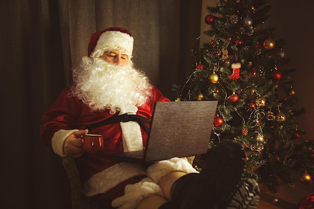 Auténtico Papá Noel está trabajando en una computadora portátil Interior de la casa