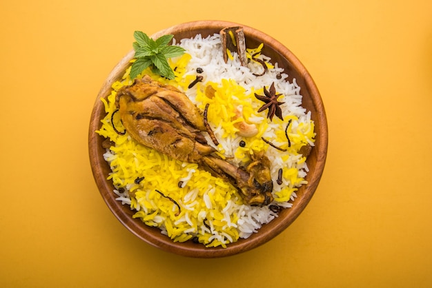 Auténtico pollo Biryani servido en un cuenco o plato sobre fondo colorido o de madera. Es una receta deliciosa de arroz basmati mezclado con pollo adobado picante servido con ensalada. Enfoque selectivo