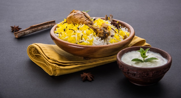 Auténtico pollo Biryani servido en un cuenco o plato sobre fondo colorido o de madera. Es una receta deliciosa de arroz basmati mezclado con pollo adobado picante servido con ensalada. Enfoque selectivo