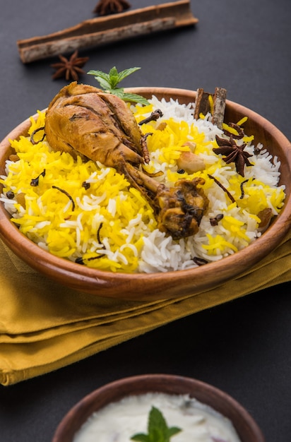 Auténtico pollo Biryani servido en un cuenco o plato sobre fondo colorido o de madera. Es una receta deliciosa de arroz basmati mezclado con pollo adobado picante servido con ensalada. Enfoque selectivo