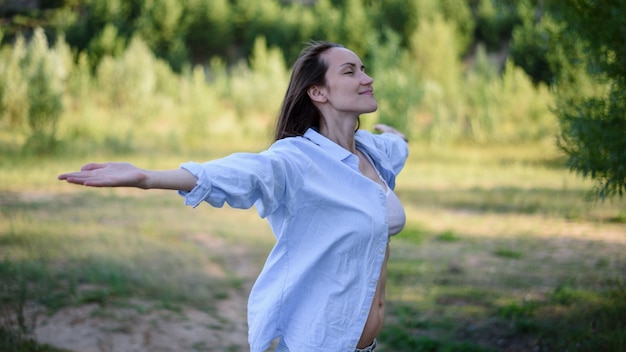 Auténtico retrato de una mujer sonriente con camisa azul con los brazos abiertos y los ojos cerrados en la naturaleza, sensación de concepto de vuelo libre