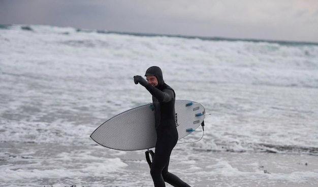 Autêntico surfista do Ártico local indo pela praia depois de surfar no mar do Norte. Litoral do mar norueguês. Esportes radicais de atividades aquáticas de inverno