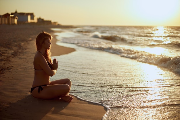 Authentische Frau im Badeanzug, die morgens Yoga Padmasana am Strand macht, echte unberührte Form