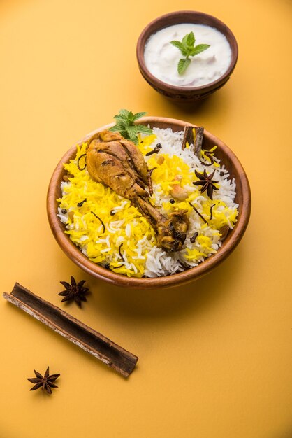 Authentisches Chicken Biryani serviert in einer Schüssel oder auf einem Teller auf buntem oder hölzernem Hintergrund. Es ist ein köstliches Rezept aus Basmatireis, gemischt mit würzig mariniertem Hühnchen, serviert mit Salat. Selektiver Fokus