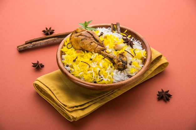 Authentisches Chicken Biryani serviert in einer Schüssel oder auf einem Teller auf buntem oder hölzernem Hintergrund. Es ist ein köstliches Rezept aus Basmatireis, gemischt mit würzig mariniertem Hühnchen, serviert mit Salat. Selektiver Fokus