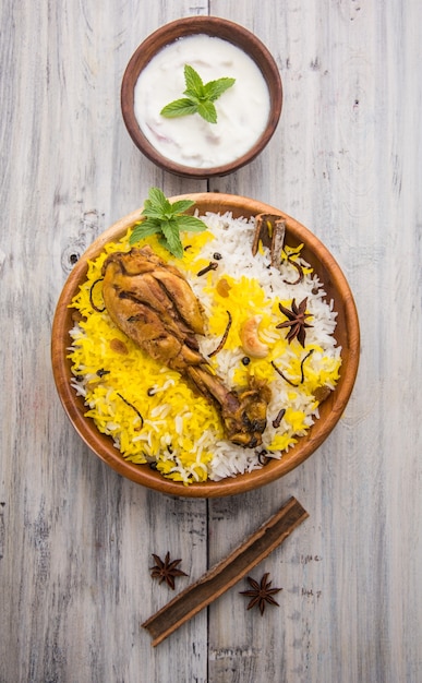 Authentisches Chicken Biryani serviert in einer Schüssel oder auf einem Teller auf buntem oder hölzernem Hintergrund. Es ist ein köstliches Rezept aus Basmatireis, gemischt mit würzig mariniertem Hühnchen, serviert mit Salat. Selektiver Fokus