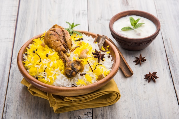 Authentisches Chicken Biryani serviert in einer Schüssel oder auf einem Teller auf buntem oder hölzernem Hintergrund. Es ist ein köstliches Rezept aus Basmatireis, gemischt mit würzig mariniertem Hühnchen, serviert mit Salat. Selektiver Fokus