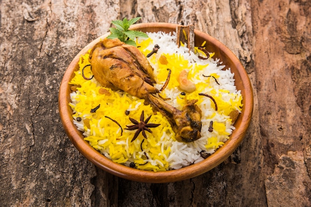 Authentisches Chicken Biryani serviert in einer Schüssel oder auf einem Teller auf buntem oder hölzernem Hintergrund. Es ist ein köstliches Rezept aus Basmatireis, gemischt mit würzig mariniertem Hühnchen, serviert mit Salat. Selektiver Fokus