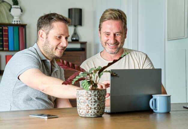 Authentisches schwules Paar, bestehend aus zwei lächelnden reifen Männern, die auf ihrem Laptop nach einem Urlaubsort suchen