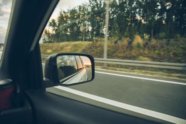 Hand nimmt tasse vom getränkehalter im auto sonnenuntergang reflexion im  autospiegel auf der autobahn