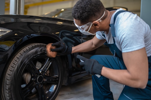 Auto-Detailer, der den schwarzen Reifenglanz mit einem Schaumschwamm auf die Radoberfläche aufträgt