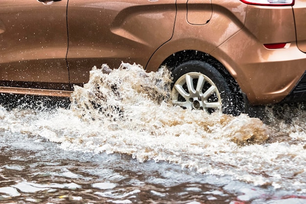 El auto está conduciendo a través de un charco bajo fuertes lluvias Salpicaduras de agua debajo de las ruedas de un auto Inundaciones y agua alta en la ciudad