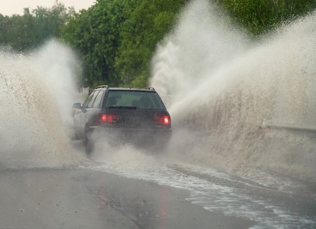 Foto auto fährt bei starkem regen in große pfütze, wasser spritzt über das auto. autofahren auf asphaltstraße bei gewitter. gefährliche fahrbedingungen