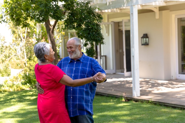 Auto-isolamento em bloqueio de quarentena. vista lateral de um casal sênior de raça mista em casa no jardim do lado de fora de sua casa em um dia ensolarado, dançando juntos e sorrindo