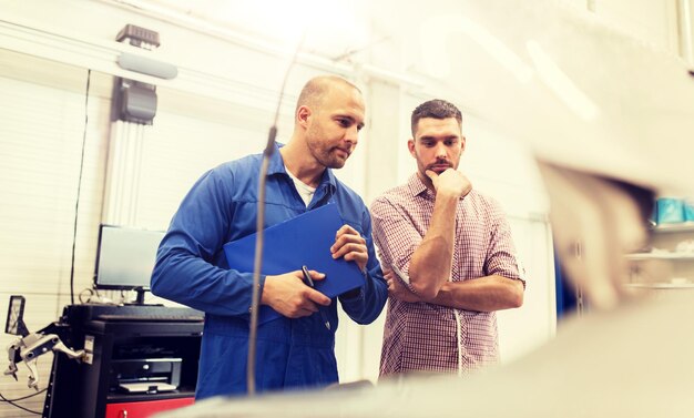 Foto auto-mechaniker mit schreibtafel und mann in der autowerkstatt