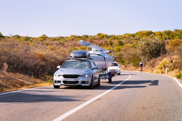 Auto mit Yacht oder Motorboot an der Straße der Costa Smeralda auf der Insel Sardinien in Italien im Sommer. Auto mit Motorboot auf der Autobahn in Europa. Blick auf Moped auf der Autobahn.