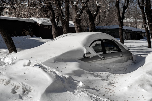 El auto plateado está en el estacionamiento en un gran banco de nieve. problemas climáticos