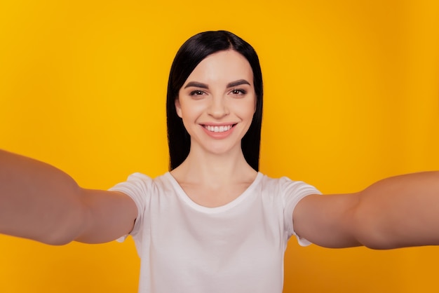 Auto-retrato de menina com dentes positivos fotografando selfie no sorriso da câmera frontal isolado em fundo amarelo