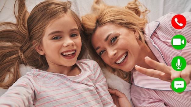 Auto-retrato de uma jovem mãe e sua filha sorrindo e olhando para a câmera durante a videochamada