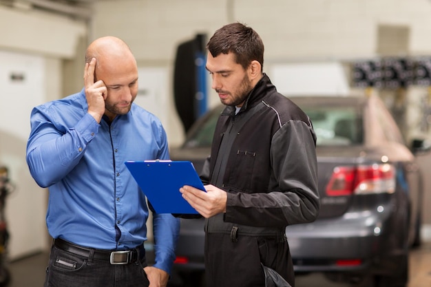 Foto auto-service-reparatur, wartung und menschenkonzept mechaniker mit klammern und kunden oder autobesitzer in der werkstatt