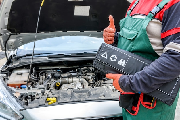 Auto-Service-Werbung. Mechaniker, der nahe Auto steht, zeigt Daumen nach oben. Auto mit geöffneter Motorhaube