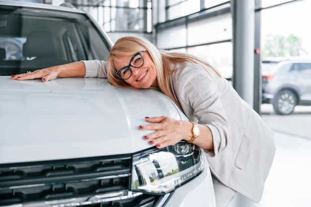 Foto auto umarmen frau in weißer abendgarderobe steht im autohaus