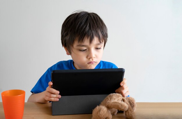 Autoaislamiento de niños usando una tableta para su tarea o estudiando una lección en línea