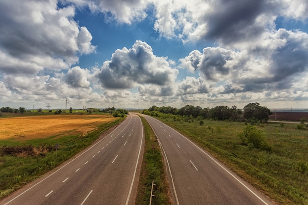 Autobahn von der Höhe der Brücke, vor dem Hintergrund von Wolken, Feldern und blauem Himmel