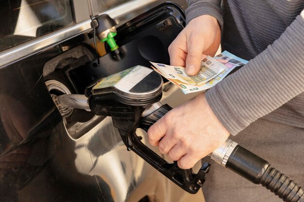 Foto autobetankung an der tankstelle mann, der auto mit kraftstoff auffüllt und geld euro hält nahaufnahme benzin-diesel wird teurer benzinindustrie und -service benzinpreis und ölkrise