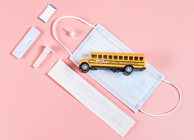 Foto un autobús escolar y una prueba rápida de covid con una máscara médica se encuentran diagonalmente en un fondo rosa