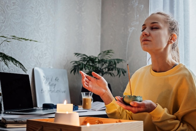 Autocuidado salud mental mujer joven sentada cerca de la mesa con luces velas palos de aroma disfrutar